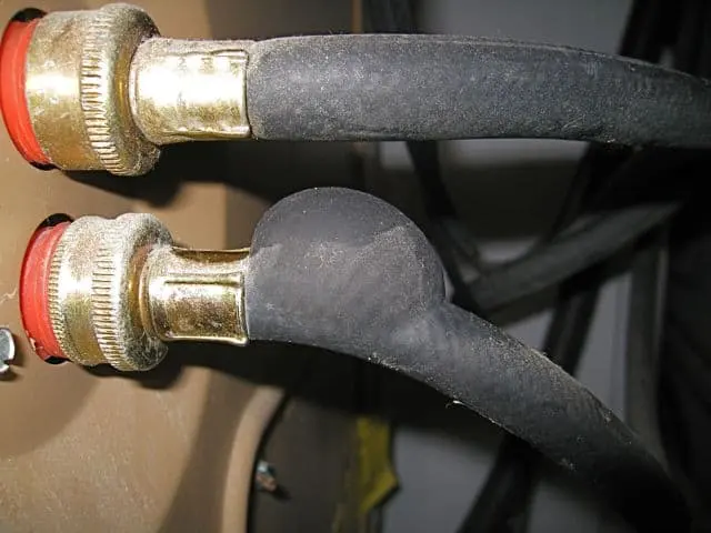 Rubber washing machine supply hoses with brass fittings behind a washer