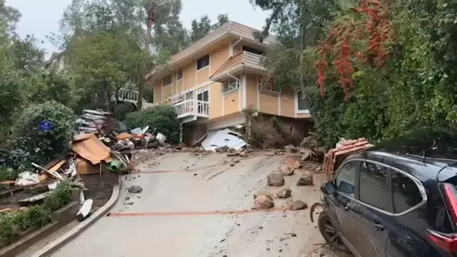 Mud and storm debris across a hillside street in front of a two-story home